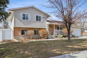 Tri-level home featuring a garage, brick siding, a front lawn, and fence