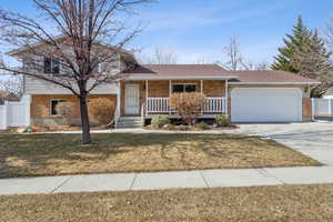 Split level home featuring brick siding, a porch, concrete driveway, a front yard, and a garage