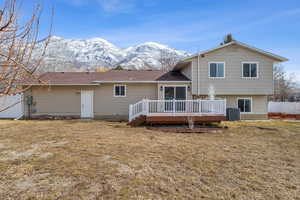 Rear view of house featuring a deck with mountain view, fence, central AC, and a yard