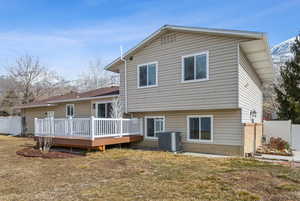 Back of house featuring a deck, a lawn, cooling unit, and fence