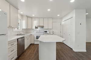 Kitchen featuring under cabinet range hood, white appliances, a kitchen island, a sink, and light countertops