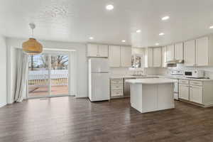 Kitchen featuring white appliances, decorative light fixtures, light countertops, under cabinet range hood, and white cabinetry