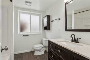 Bathroom featuring baseboards, a shower, toilet, wood finished floors, and vanity