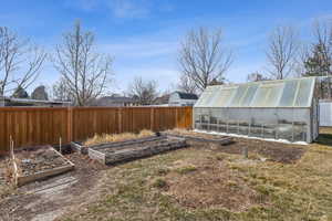 View of yard with a garden, a fenced backyard, a greenhouse, and an outbuilding