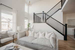 Living area with a towering ceiling, an inviting chandelier, wood finished floors, baseboards, and stairs