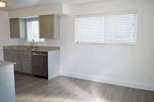 Kitchen with baseboards, dishwasher, light stone counters, wood finished floors, and a sink