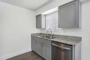 Kitchen featuring dark wood-type flooring, a sink, baseboards, gray cabinets, and dishwasher