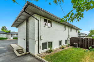 Rear view of house with a yard, brick siding, fence, and central AC unit