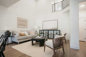 Living room with recessed lighting, wood finished floors, a towering ceiling, and baseboards