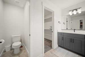 Bathroom with toilet, a spacious closet, vanity, and visible vents