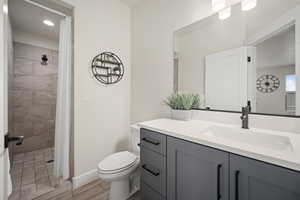 Bathroom featuring toilet, a tile shower, vanity, and baseboards