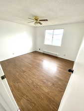 Spare room with a textured ceiling, baseboard heating, and wood finished floors