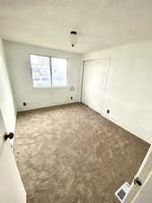 Spare room featuring a textured ceiling, carpet floors, and visible vents