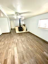 Unfurnished living room with ceiling fan, a textured ceiling, baseboards, light wood finished floors, and a wood stove