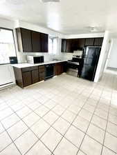 Kitchen with dark brown cabinetry, black appliances, light countertops, and a sink