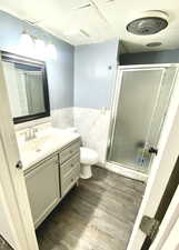 Full bath with tile walls, a stall shower, wainscoting, vanity, and wood finished floors