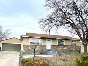 Ranch-style home featuring stone siding, a fenced front yard, a detached garage, and stucco siding