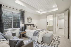 Bedroom featuring a tray ceiling, light carpet, ensuite bath, wooden ceiling, and baseboards