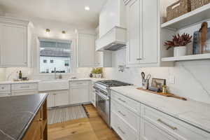 Kitchen featuring open shelves, white cabinetry, high end range, and a sink