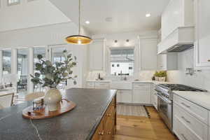 Kitchen with decorative light fixtures, light wood-style flooring, white cabinetry, a sink, and high end stove