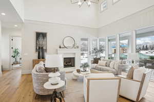 Living room featuring light wood-type flooring, a notable chandelier, a fireplace, and a towering ceiling