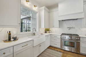 Kitchen with a sink, white cabinets, high end stainless steel range, backsplash, and light stone countertops