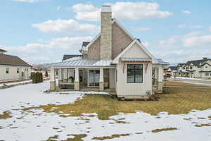 Snow covered house with a chimney, a porch, board and batten siding, a standing seam roof, and metal roof