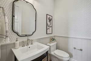 Bathroom with a wainscoted wall, a sink, toilet, and wallpapered walls