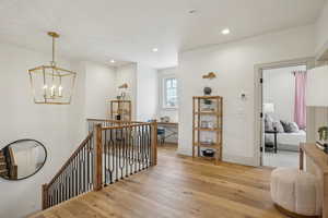 Corridor featuring recessed lighting, light wood-style flooring, an inviting chandelier, an upstairs landing, and baseboards