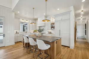 Kitchen with white cabinets, a kitchen island, a kitchen breakfast bar, hanging light fixtures, and light wood-type flooring