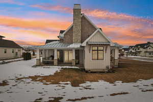 Snow covered house with metal roof, a porch, board and batten siding, a standing seam roof, and a chimney