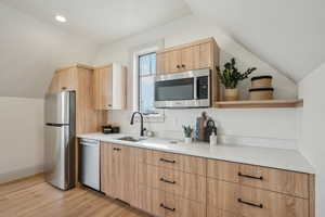 Kitchen with modern cabinets, appliances with stainless steel finishes, vaulted ceiling, open shelves, and a sink