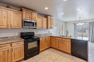 Kitchen with black appliances, pendant lighting, a sink, and light tile patterned flooring