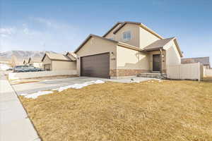 View of front of home with concrete driveway, a front yard, fence, a mountain view, and stone siding