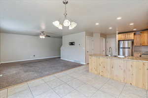 Kitchen featuring visible vents, freestanding refrigerator, light stone countertops, light brown cabinets, and a sink