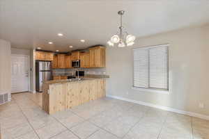 Kitchen featuring stainless steel appliances, an inviting chandelier, a sink, light stone countertops, and a peninsula