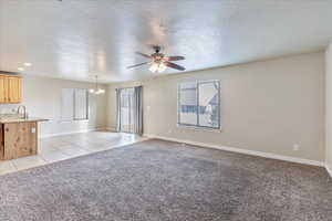 Unfurnished living room with light tile patterned floors, light colored carpet, a sink, baseboards, and ceiling fan with notable chandelier