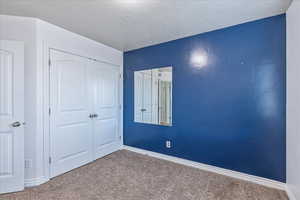 Unfurnished bedroom featuring a textured ceiling, a closet, carpet, and baseboards