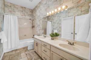 Full bath with toilet, double vanity, a sink, and shower / tub combo with curtain