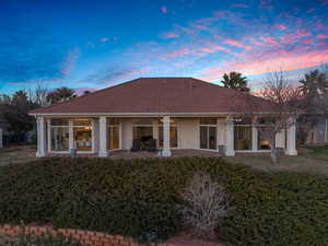 Back of property at dusk with stucco siding, a tile roof, a patio, and a yard