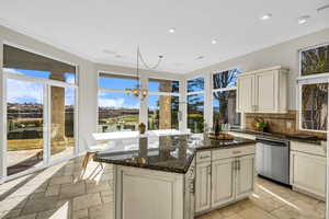 Kitchen with dark stone counters, stainless steel dishwasher, decorative light fixtures, and crown molding