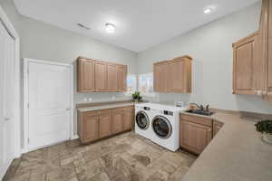 Laundry area featuring visible vents, washing machine and clothes dryer, a sink, and cabinet space