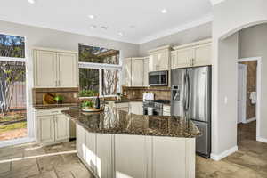 Kitchen with stainless steel appliances, a kitchen island, dark stone countertops, stone tile flooring, and crown molding