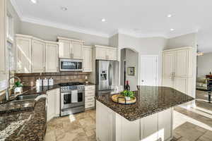 Kitchen featuring dark stone counters, a kitchen island, backsplash, stainless steel appliances, and a sink