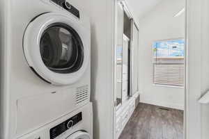 Clothes washing area featuring laundry area, visible vents, baseboards, stacked washing maching and dryer, and dark wood-style floors