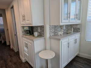 Kitchen with light countertops, tasteful backsplash, dark wood-type flooring, and white cabinetry