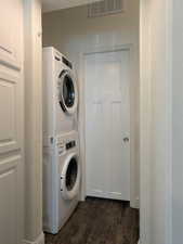 Laundry room with laundry area, dark wood-type flooring, stacked washer / dryer, and visible vents