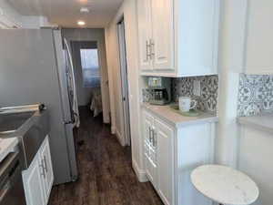 Kitchen featuring dark wood-style flooring, white cabinets, light countertops, freestanding refrigerator, and decorative backsplash