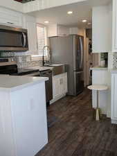 Kitchen featuring white cabinets, stainless steel appliances, dark wood-type flooring, and stacked washer and clothes dryer