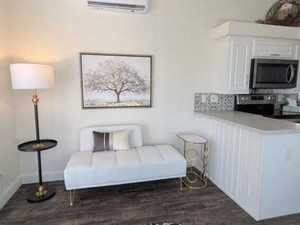 Living area with dark wood-style floors, a wall mounted air conditioner, and baseboards